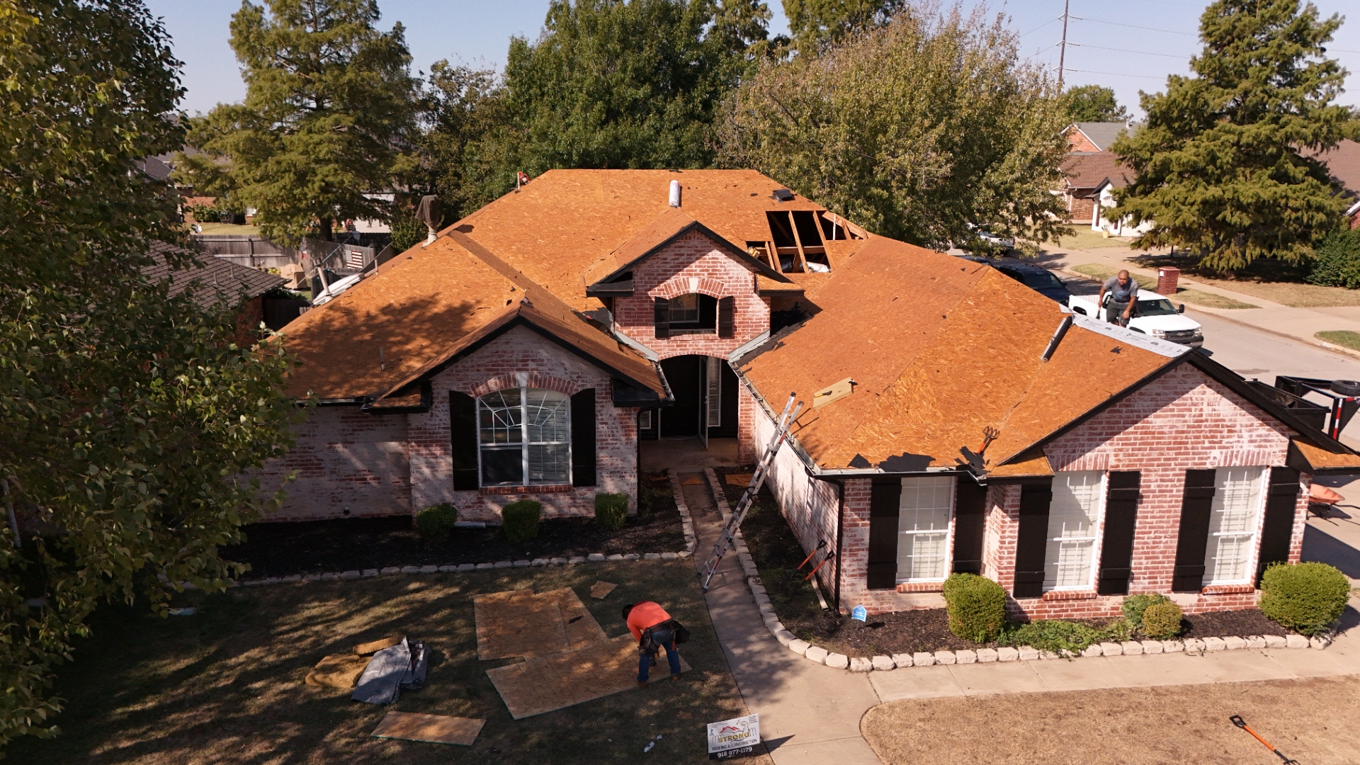 Aerial view of active residential roof replacement showing crew working on decking